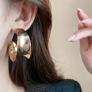 Close-up of bold wide metal earrings with gold finish, showing premium texture on ear