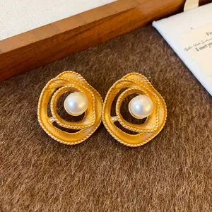 Close-up of vintage gold-tone spiral stud earrings with elegant faux pearl center.