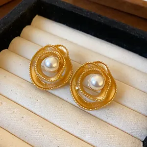 Close-up view of vintage golden spiral stud earrings with white faux pearls in a box