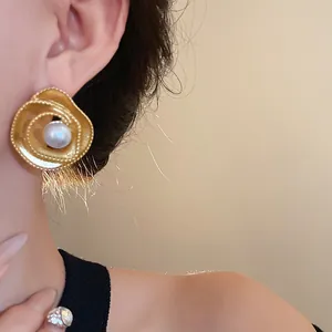 Vintage-style spiral golden stud earrings with central faux pearl on model