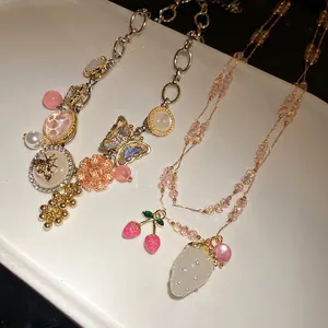 Ornate crystal pendant necklaces with bee and strawberry charms on white tray