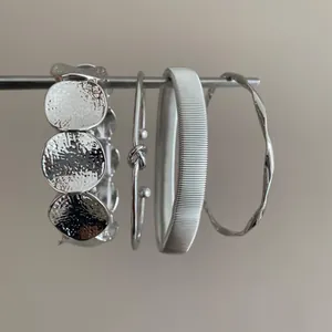 Minimalist set of silver geometric metal bracelets with textured and knotted designs.
