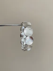 Close-up of silver-tone metal bracelet showing irregular round disc texture