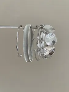 Close-up side view detail of textured silver geometric metal bangles and bracelets set.
