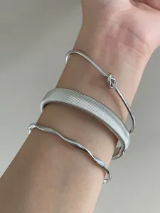 Close-up of stacked silver geometric open bangles with various textures on wrist