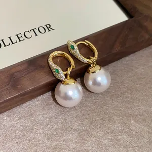 Close-up detail of elegant gold snake earrings with pave diamonds and white pearl drops.