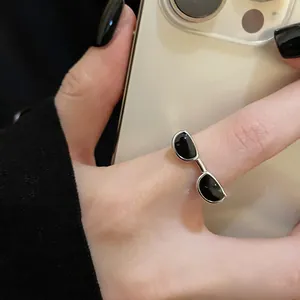 Dettaglio ravvicinato di un anello aperto color argento con un design creativo a occhiali da sole.