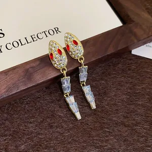 Detail of gold-tone snake earrings with sparkling white crystals and red gemstone eyes.