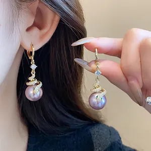 Detailed macro view of elegant gold snake-shaped earrings featuring purple pearls and rhinestones