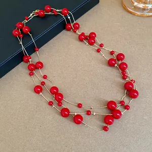 Detail showing a layered vintage necklace with vibrant red round beads on gold-toned chains.