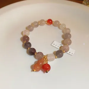 Close-up of handmade beaded bracelet with strawberry quartz and gourd pendant on white plate.