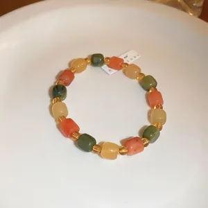 Detailed view of a handmade beaded bracelet with multi-colored stone beads on a white dish.