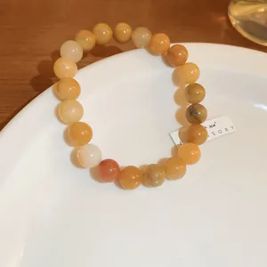 Detail of a warm yellow and orange elastic beaded strawberry quartz bracelet on a white plate