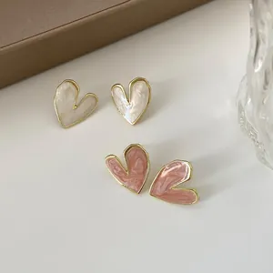 Close-up of heart-shaped enamel stud earrings with gold trim and marble texture.