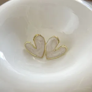 Close-up of heart-shaped earrings with golden edges and cream pearlescent drip oil finish