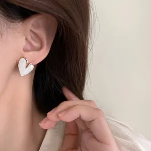 Close-up of white heart-shaped enamel stud earrings with gold trim on ear.