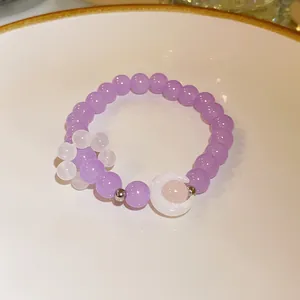 Handmade purple beaded bracelet with a white crescent moon charm on a ceramic plate