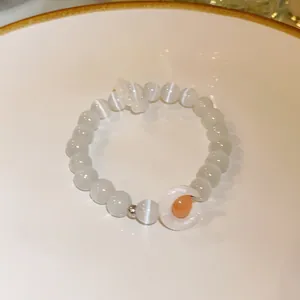 Close-up of white cat-eye beaded bracelet featuring a crescent moon and orange bead charm.