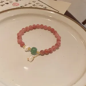 Detailed close-up of a strawberry quartz beaded bracelet with pearl and green jade charms