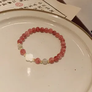 Detailed view of handmade strawberry quartz bracelet with a white carved rose charm