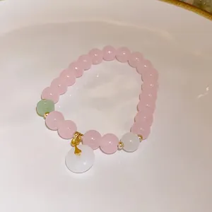 Close-up of a handmade pink strawberry quartz beaded bracelet with a white donut charm