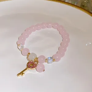Close-up view of a pink strawberry crystal beaded bracelet with a gold heart key charm