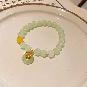 Detail of a New Chinese style beaded bracelet with green jade-like beads and a gold charm