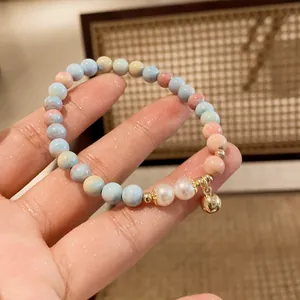 Close-up detail of handmade beaded bracelet with pearls and a gold bell charm