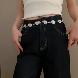 Detailed view of a bohemian silver seashell chain belt worn on dark blue denim jeans