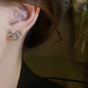 Close-up view of a unique cyberpunk cat head stud earring featuring a delicate dangling chain