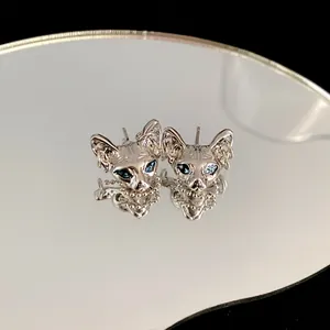 Detailed macro view of silver cyberpunk cat head earrings with blue gemstone eyes
