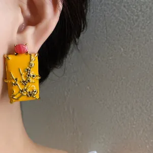Close-up detail of new Chinese style yellow enamel square earrings with floral branch decoration.