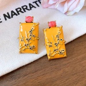Detail showing yellow enamel rectangular earrings with gold floral relief and red stone