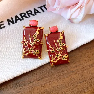 Close-up of New Chinese style red enamel earrings with gold floral branch details.