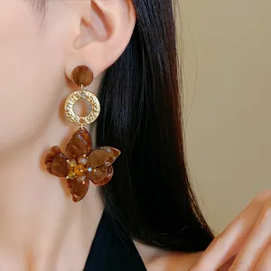 Close-up of elegant brown marbled floral dangle earrings with gold accents worn on an ear.