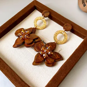 Close-up of brown acetate flower earrings with gold textured rings and crystals.