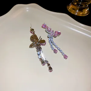 Close-up of elegant butterfly tassel earrings with sparkling pink zircons on a tray.