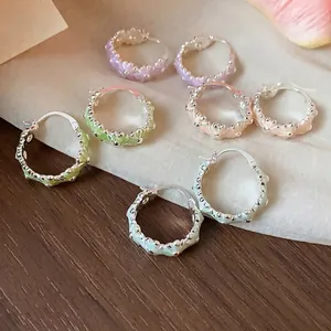 Elegant sweet floral enamel hoop earrings in various pastel colors on wooden surface.