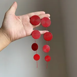 Detailed close-up of red metallic textured circular tassel earrings held by hand for scale