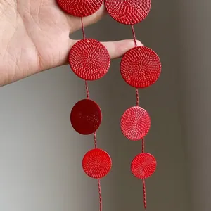 Close-up view of vibrant red textured circular metal earrings with a tiered tassel design