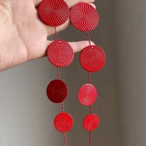 Detail showing the intricate texture of red circular disc tassel earrings held by hand
