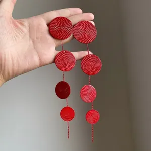 Close-up of red textured circular disks on long drop tassel earrings for women.