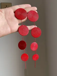 Close-up of red metal textured round disc tassel earrings held in hand