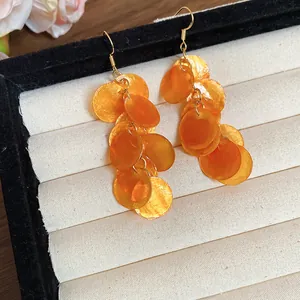 Dettaglio degli orecchini a frangia con dischi di conchiglia arancioni su un vassoio portagioie.