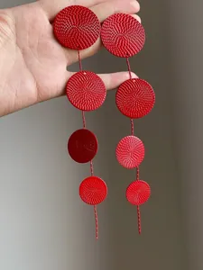 Close-up of vibrant red metal textured round disc tassel earrings held in hand.
