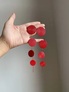 Detail view of red circular earrings with textured metal surface and long fringe