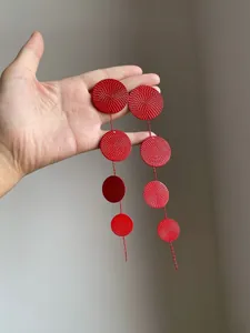 Detailed view of red round metal earrings with spiral textured surface held by hand.