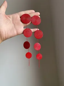 Close-up of vibrant red textured round disc tassel earrings with detailed surface patterns.