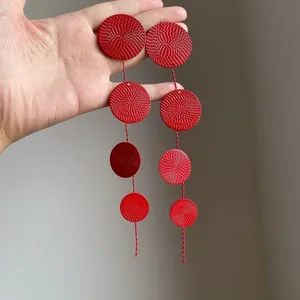 Macro detail of red textured circular dangle earrings with a tiered disc design