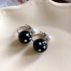 Vista dettagliata di orecchini retrò in resina nera a pois bianchi e perle eleganti.